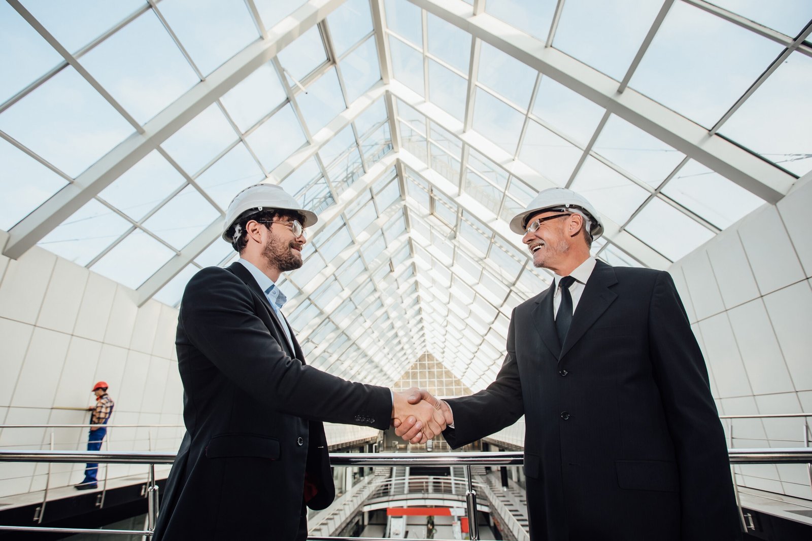 two cheerful businessman handshaking helmet new building scaled